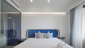 A hotel room with a large bed, a headboard, a bedside table, a shower area, and a window with curtains. - M Gallery Apartment Phu Quoc (Phu Quoc)