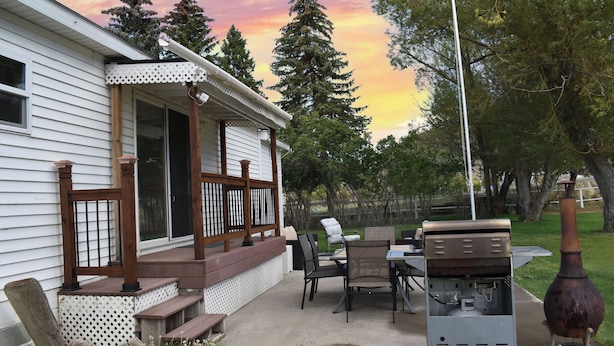 Un porche cubierto con mobiliario exterior, una parrilla y una chimenea decorativa.