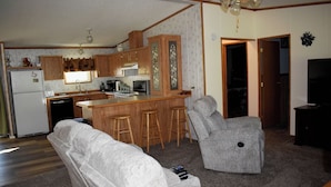 Un espacio habitable compacto con kitchenette, un sillón gris, un sofá y una pequeña zona de bar.