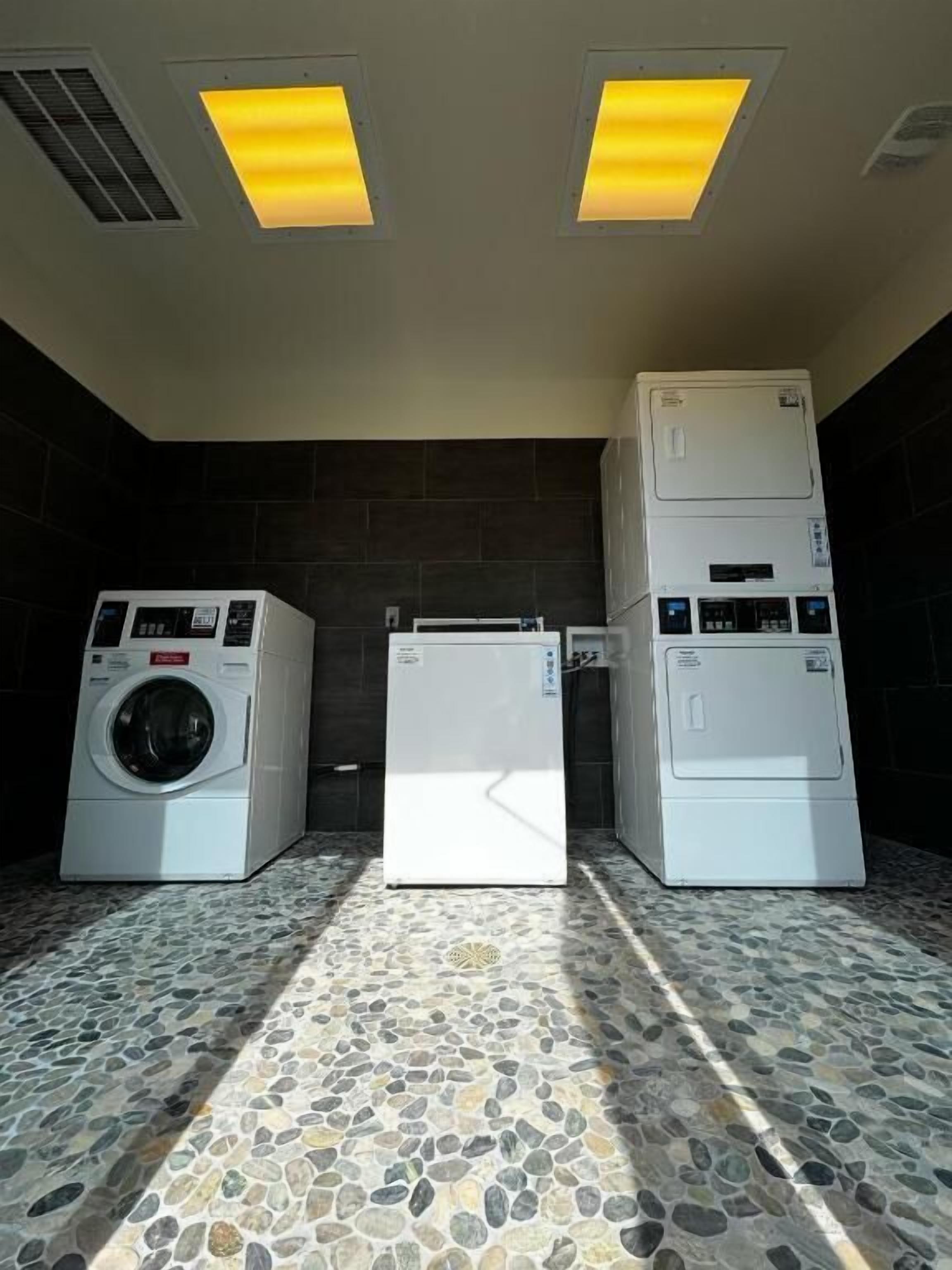 A laundry room with three stacked washers and dryers, a tiled floor, and overhead lighting.