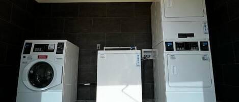 A laundry room with three stacked washers and dryers, a tiled floor, and overhead lighting.