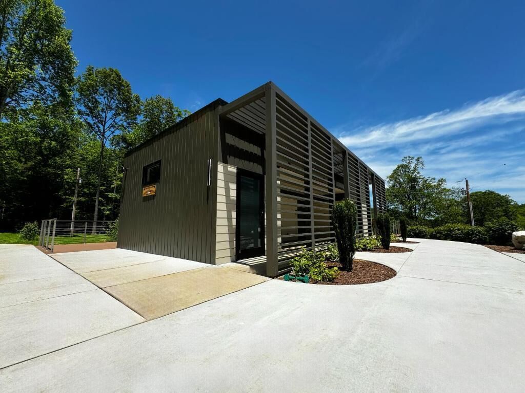 Un bâtiment moderne doté d’un toit en pente et de grandes fenêtres, entouré d’une terrasse en béton et d’espaces paysagers aménagés.