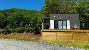Un bâtiment moderne doté d’une terrasse en bois, entouré d’une végétation luxuriante et surplombant un ciel d’un bleu éclatant.
