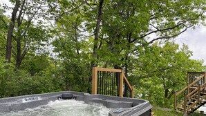 A hot tub surrounded by trees, a wooden deck, and a wooden staircase.