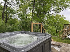 Un bain à remous entouré d’arbres, une terrasse en bois et un escalier en bois.
