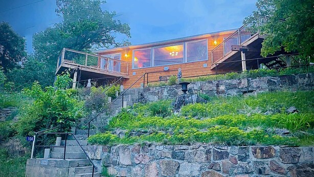 A wooden cabin with a stone staircase leading up to it, surrounded by greenery.