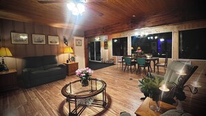 A cozy living room with a wooden ceiling, a ceiling fan, a dining area with a table and chairs, and a large window with a view.