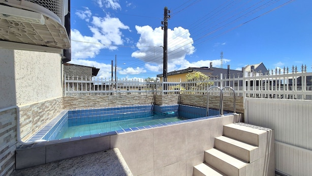 Una piscina con borde de azulejos, una cerca blanca y una escalera que lleva a ella.