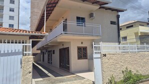 Un edificio residencial de dos pisos con un balcón, una entrada protegida por una reja y un muro de piedra.