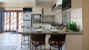 A kitchen with a dining area, white cabinets, a microwave, a stove, and green bottles on the counter. - Fully Equipped Houses in a Condominium With a Pool, 110m From the Beach - Onis (Barra Velha)