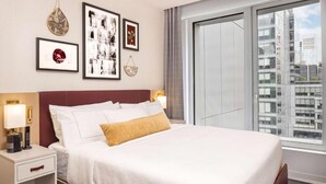Ein modernes Hotelzimmer mit einem großen Bett, einem Nachttisch mit Lampe und gerahmten Bildern an der Wand.
