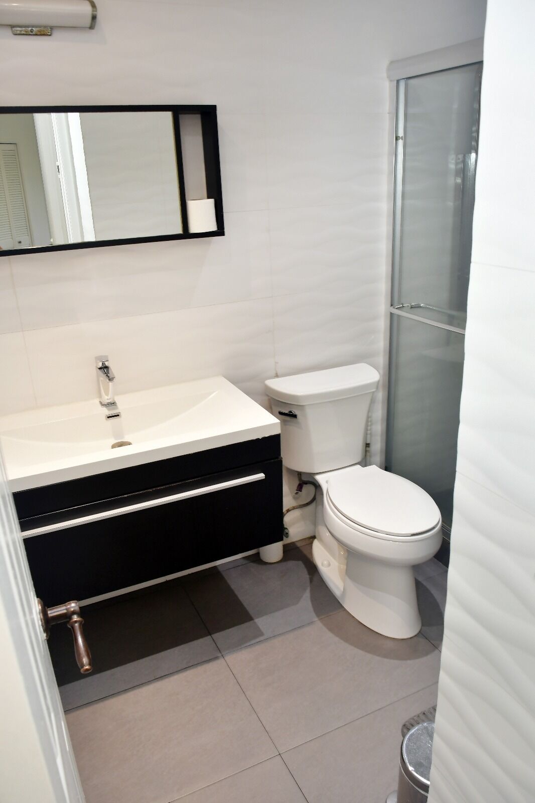 Bagno con lavandino bianco, mobile contenitore nero, WC bianco e box doccia in vetro.