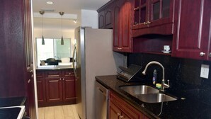 A kitchen with dark wooden cabinets, a stainless steel sink, and a refrigerator. - Modern 2-bedroom apartment in North Miami Beach with AC (North Miami Beach)
