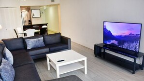 A modern living room with a sectional sofa, a white coffee table, and a large flat-screen TV on a stand. - Modern 2-bedroom apartment in North Miami Beach with AC (North Miami Beach)