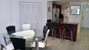 A modern kitchen with a glass dining table, bar stools, and a refrigerator. - Modern 2-bedroom apartment in North Miami Beach with AC (North Miami Beach)