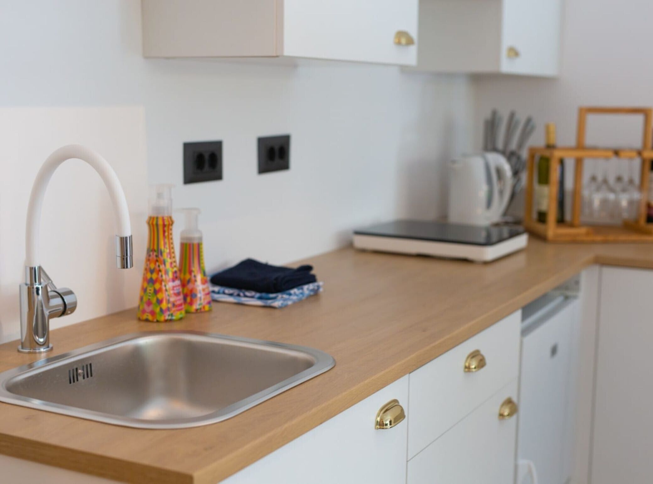 A modern kitchen with a stainless steel sink, a white countertop, and a wooden cabinet.