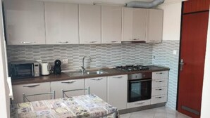 A compact kitchen with a microwave, coffee maker, sink, stove, and oven. There is a dining table with a patterned tablecloth and chairs.