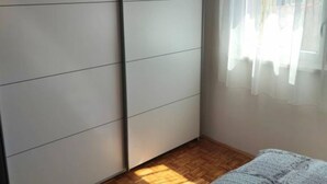 A room with a sliding wardrobe, a wooden floor, and a window with sheer curtains.