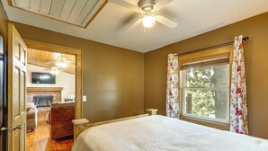 A bedroom with a bed, a ceiling fan, a window with curtains, a fireplace, and a television on the wall. - Ozarks Waterfront Home w/ Dock & Marina Access (Warsaw)