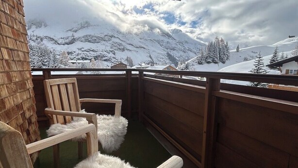 Ein Balkon mit Holzstühlen und Blick auf schneebedeckte Berge.