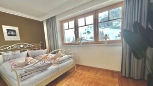 Ein Schlafzimmer mit einem Metallbettgestell, einem großen Fenster mit Blick auf schneebedeckte Bäume und einem Holzboden.