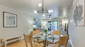 Un coin repas comprenant une table ronde en verre, six chaises en bois, un banc et un ventilateur de plafond.