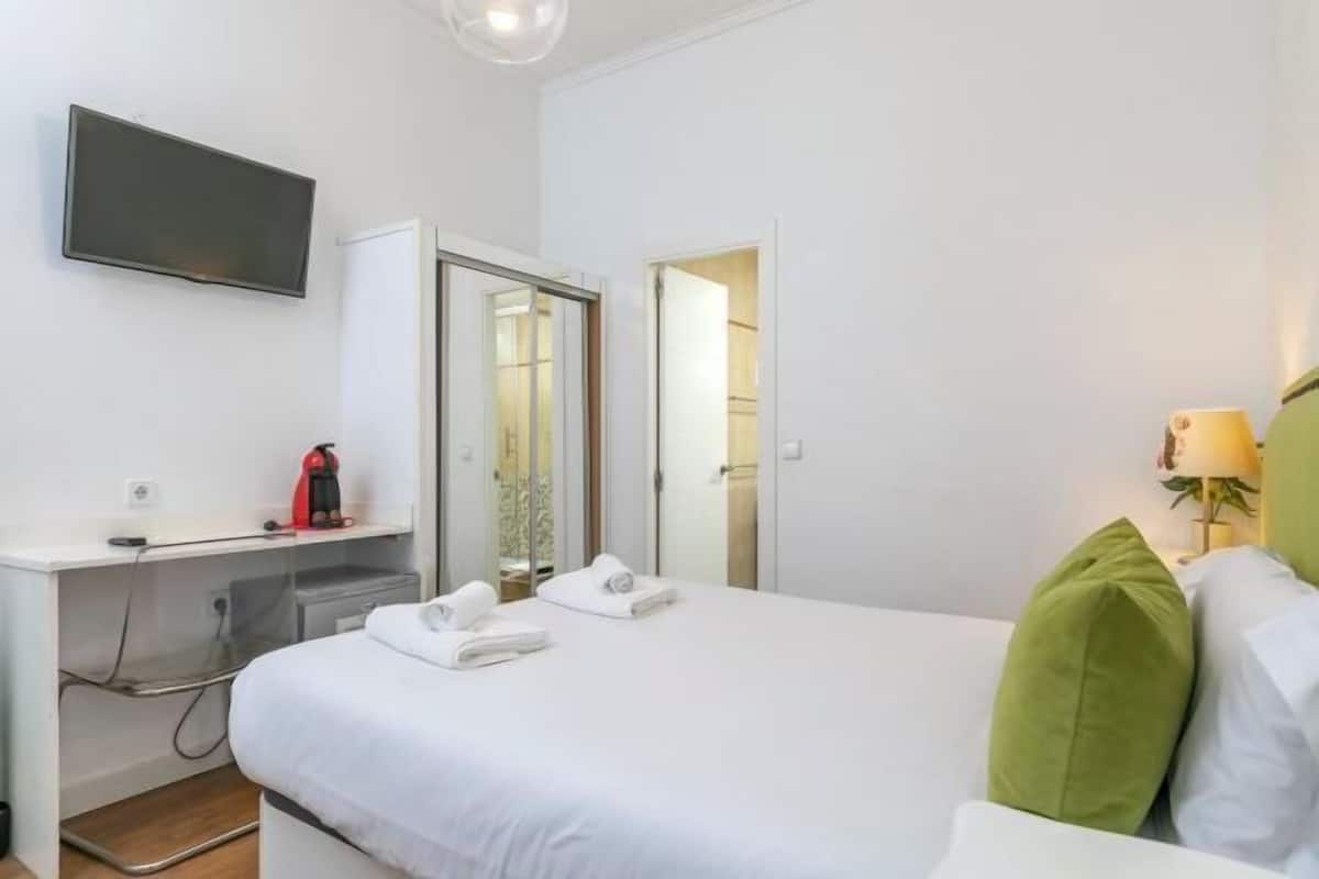 A hotel room with a bed, a desk with a computer, a TV, and a lamp.