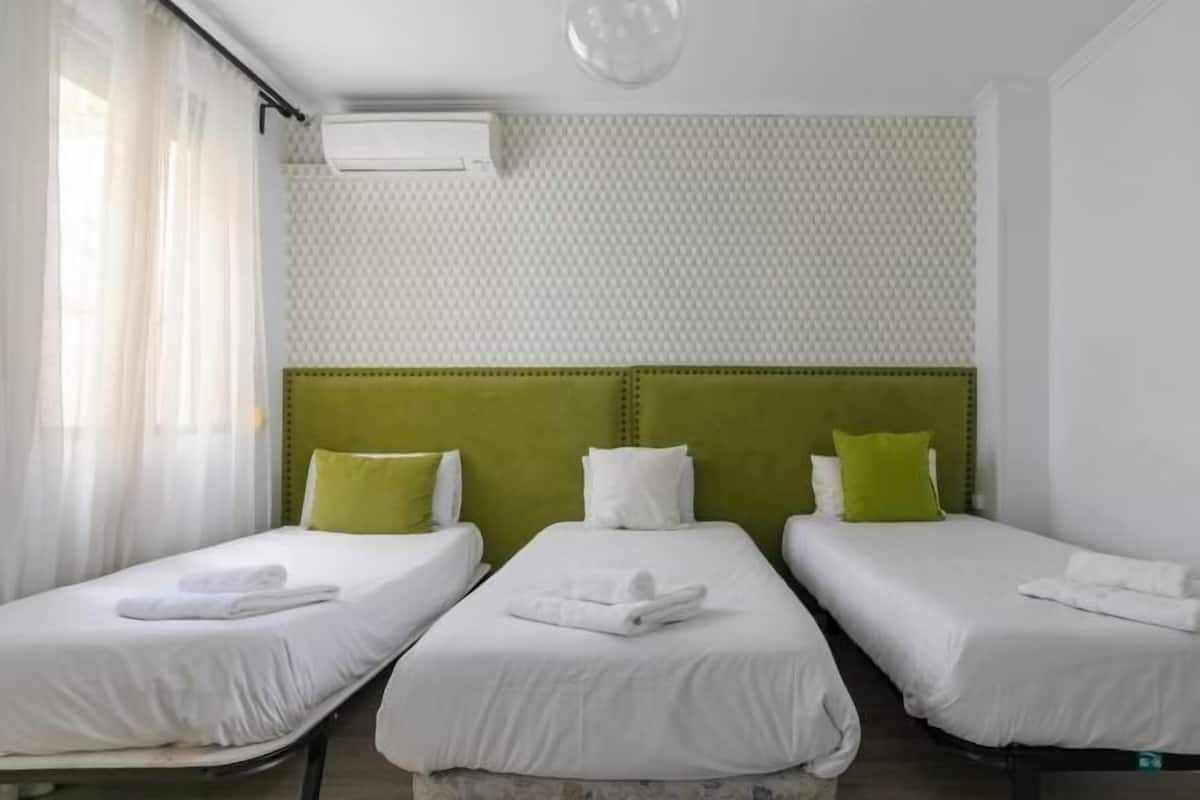 A hotel room with three single beds, each with white bedding and green pillows.