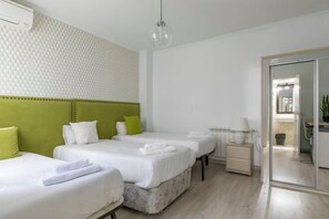 A hotel room with three beds, a green headboard, a bedside table with a lamp, and a sliding glass door to the bathroom. - H-A San Mateo Suites (Madrid)