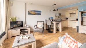 A modern living room with a TV, seating, and a dining area. - 2 Person Island View Apartment (De Koog)