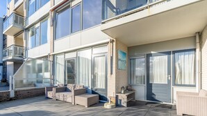 A modern building with a covered outdoor seating area, large windows, and a staircase leading to an upper level. - 2 Person Island View Apartment (De Koog)