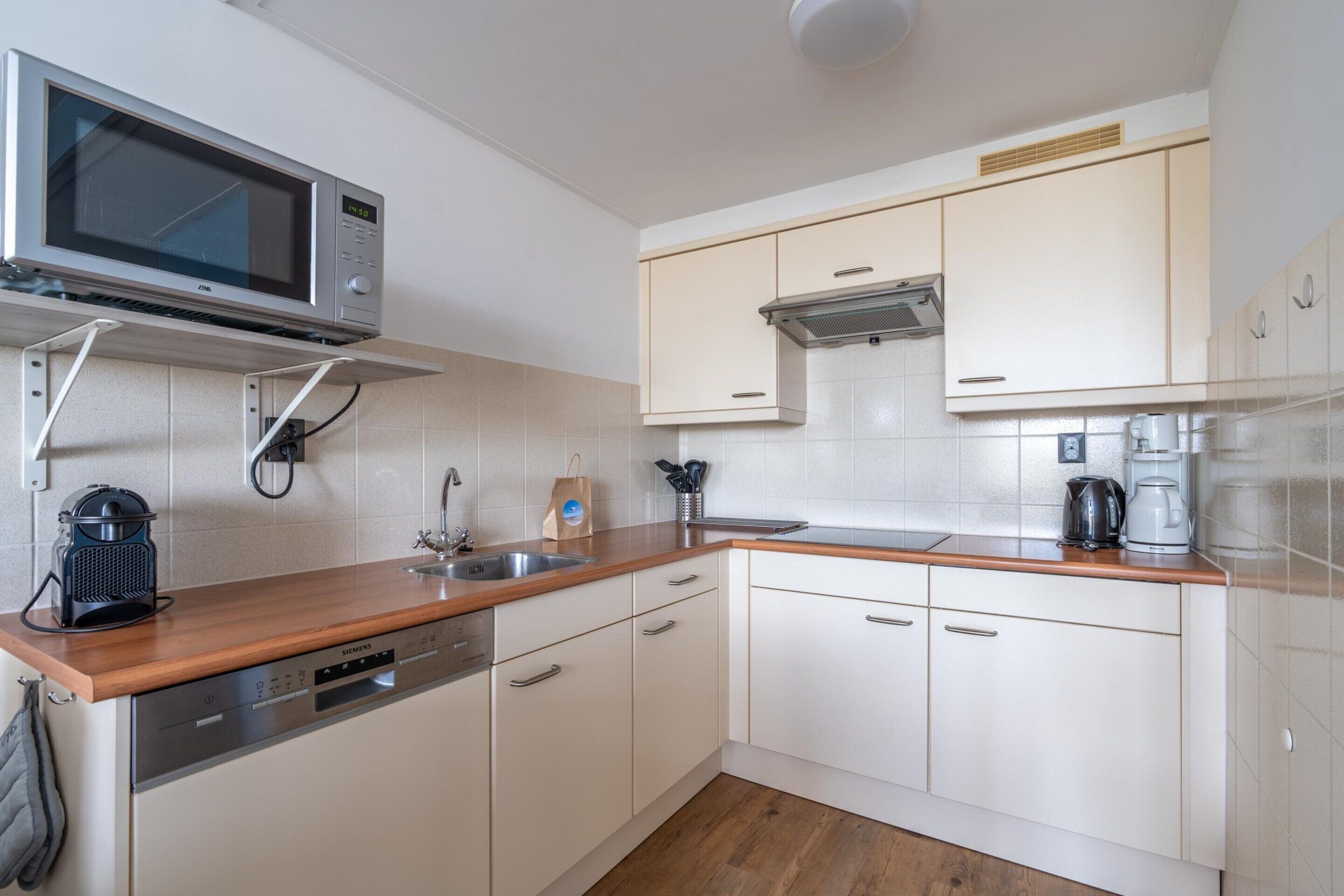 A modern kitchen with white cabinets, a stainless steel dishwasher, a microwave, and a coffee maker.