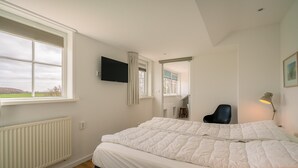 A bedroom with a bed, a TV, a chair, a desk, and a window with a view. - Tastefully Furnished Holiday Home (De Koog)
