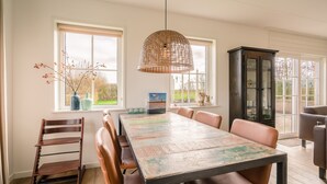 A dining area with a wooden table, leather chairs, a hanging rattan light, and a cabinet with glass doors. - Tastefully Furnished Holiday Home (De Koog)