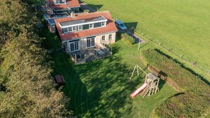 A large house with a red roof, a garden, and a swing set. - Tastefully Furnished Holiday Home (De Koog)