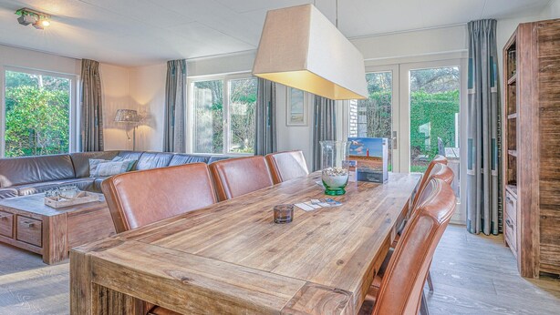 A spacious dining area with a wooden table and leather chairs, large windows with curtains, and a view of greenery outside. - Charming Villa Near the sea and Forest (De Koog)