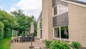 A modern house with a brick exterior, large windows, and a patio with outdoor furniture. - Charming Villa Near the sea and Forest (De Koog)