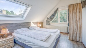 A bedroom with two beds, a skylight, a nightstand with a lamp, and a wardrobe. - Charming Villa Near the sea and Forest (De Koog)