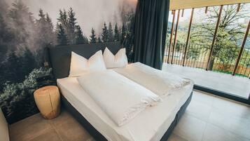 Une chambre moderne avec un grand lit, une vue sur les arbres par la fenêtre et un balcon.