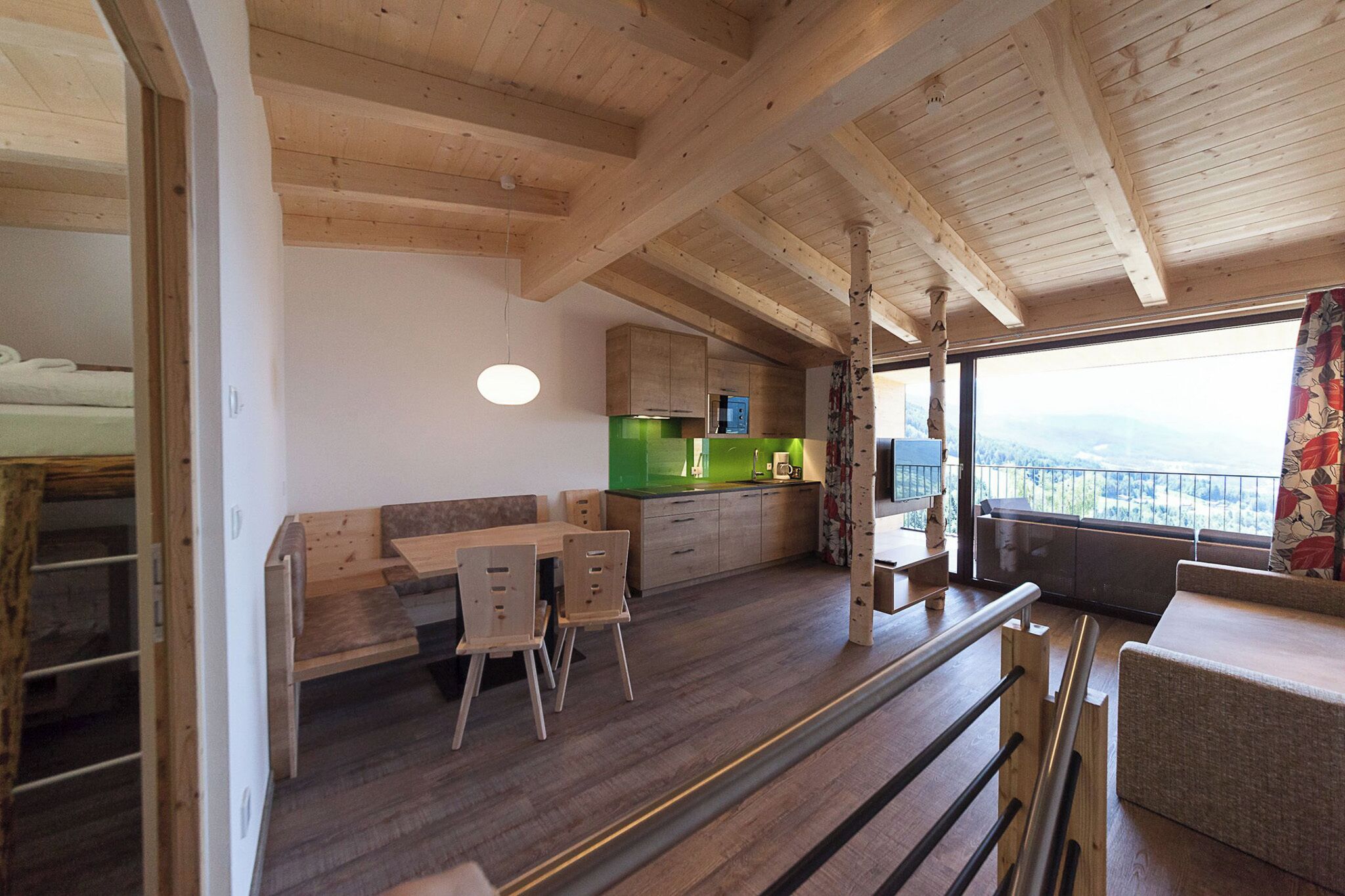 Interior de madera con comedor, cocina y balcón con vistas.