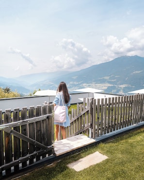 A person standing on a wooden deck overlooking a mountainous landscape.