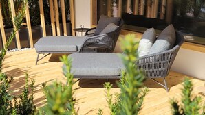 A sunlit outdoor seating area with wicker furniture and a glass door leading to a garden. - Aparthotel Bacher (Bressanone)