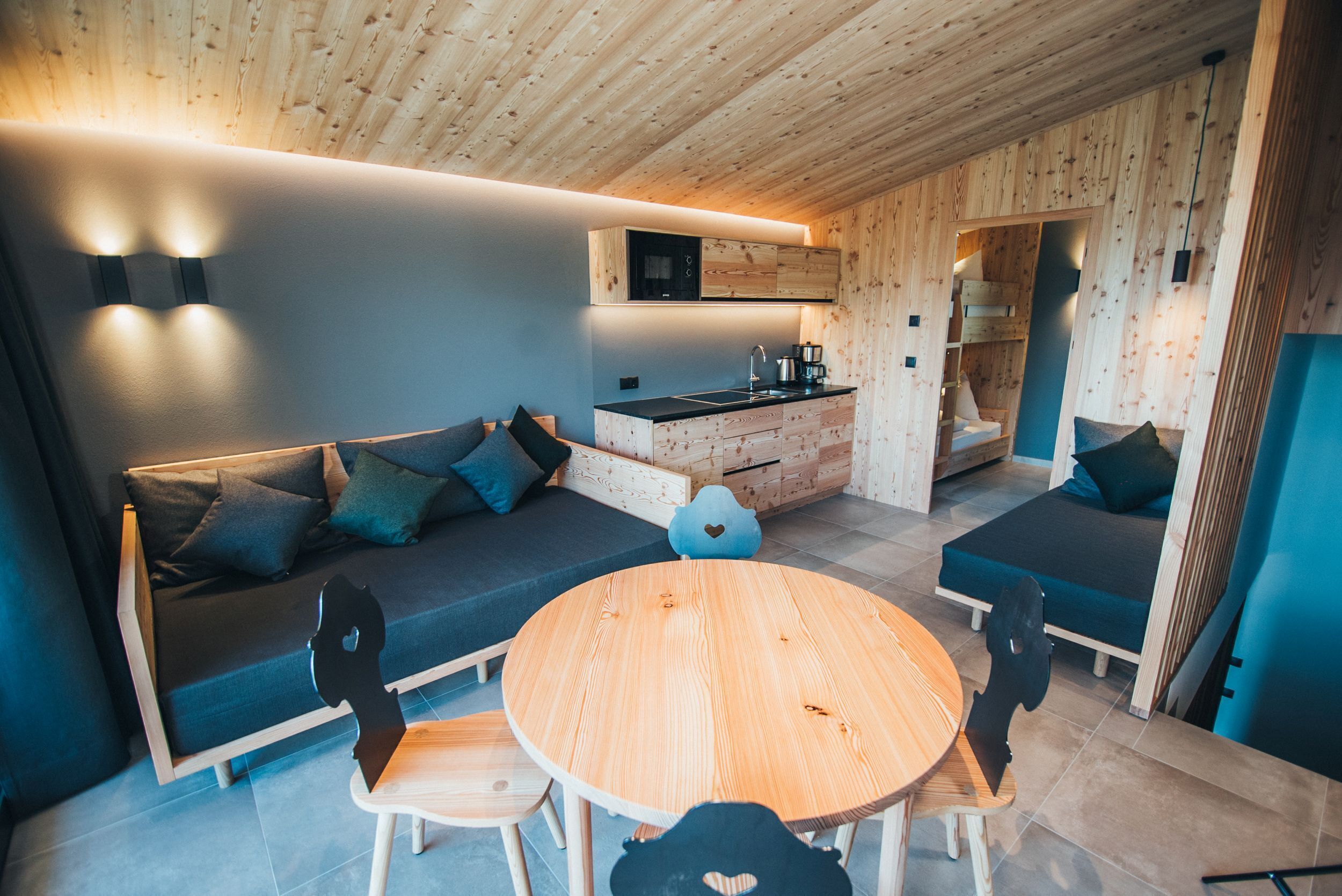 A compact living space with a sofa, a round wooden table, and a kitchenette.