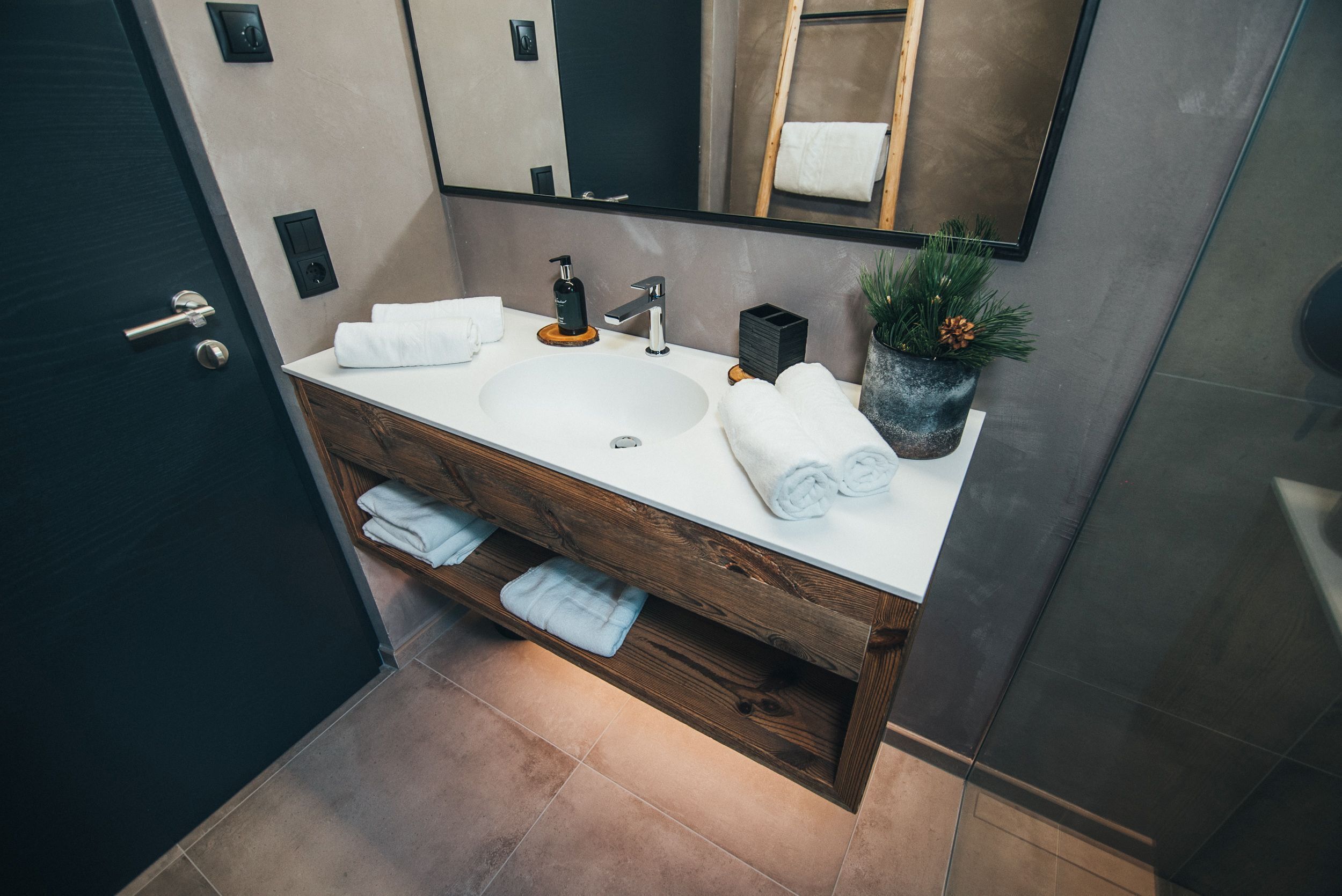 Een moderne badkamer met een houten wastafelmeubel, een grote spiegel en een kamerplant.