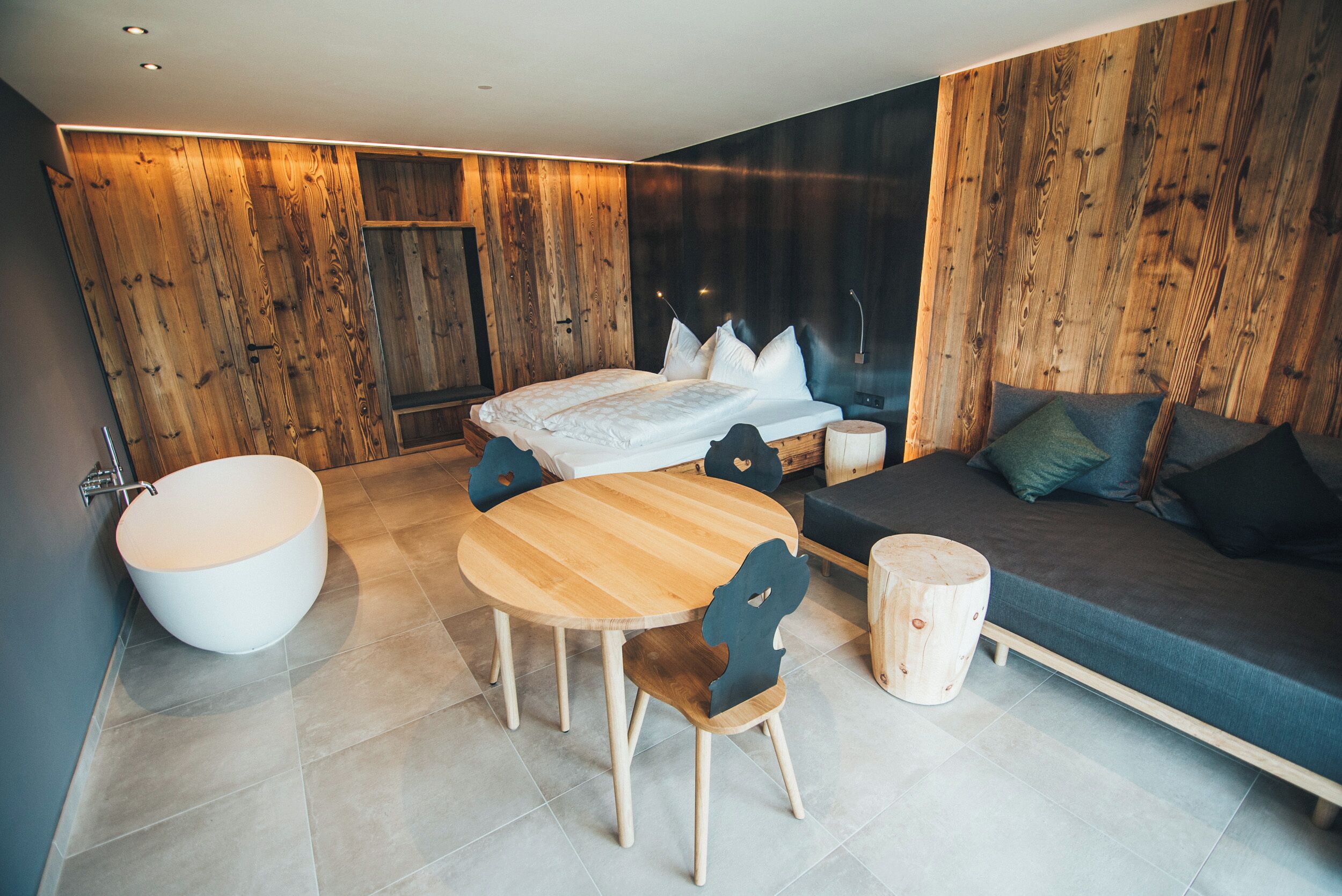A modern bedroom with a large bed, a round wooden table, and a built-in bathtub.