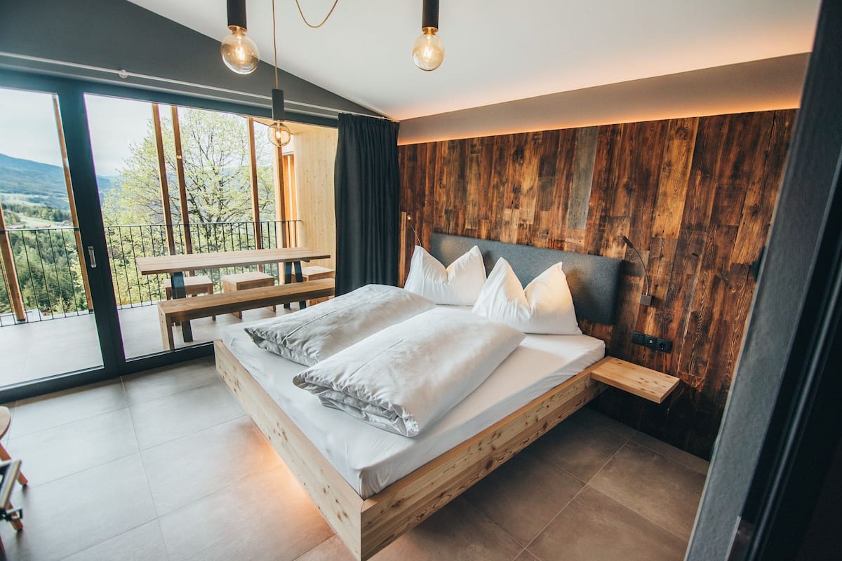 A modern bedroom with a wooden bed, large windows, and a view of the outdoors.