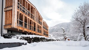 A modern wooden building with balconies, surrounded by snow-covered trees and mountains. - Aparthotel Bacher (Bressanone)