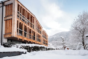 A modern wooden building with balconies, surrounded by snow-covered trees and mountains.