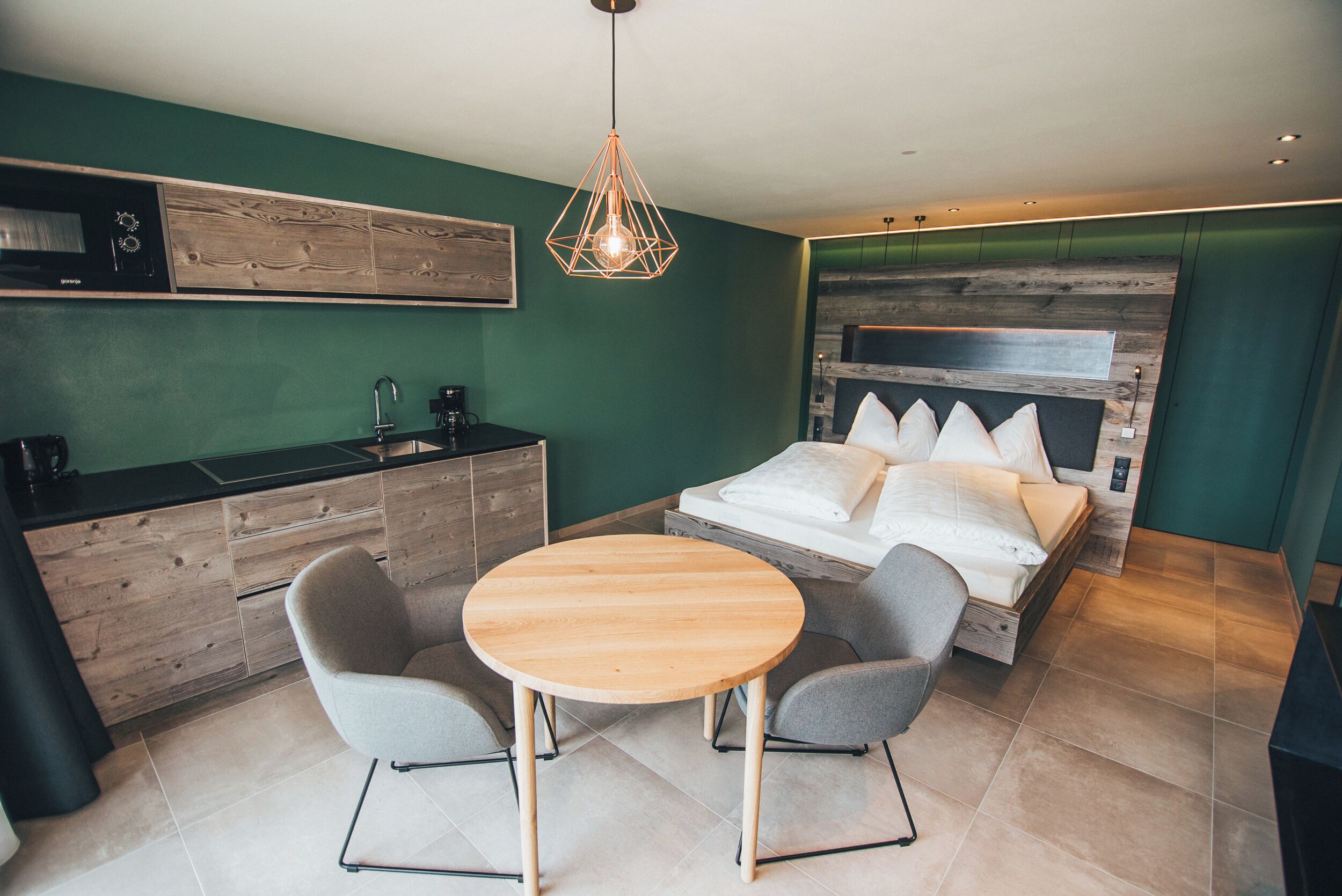 Una habitación pequeña con cama, una kitchenette compacta y una mesa redonda de madera con dos sillas.