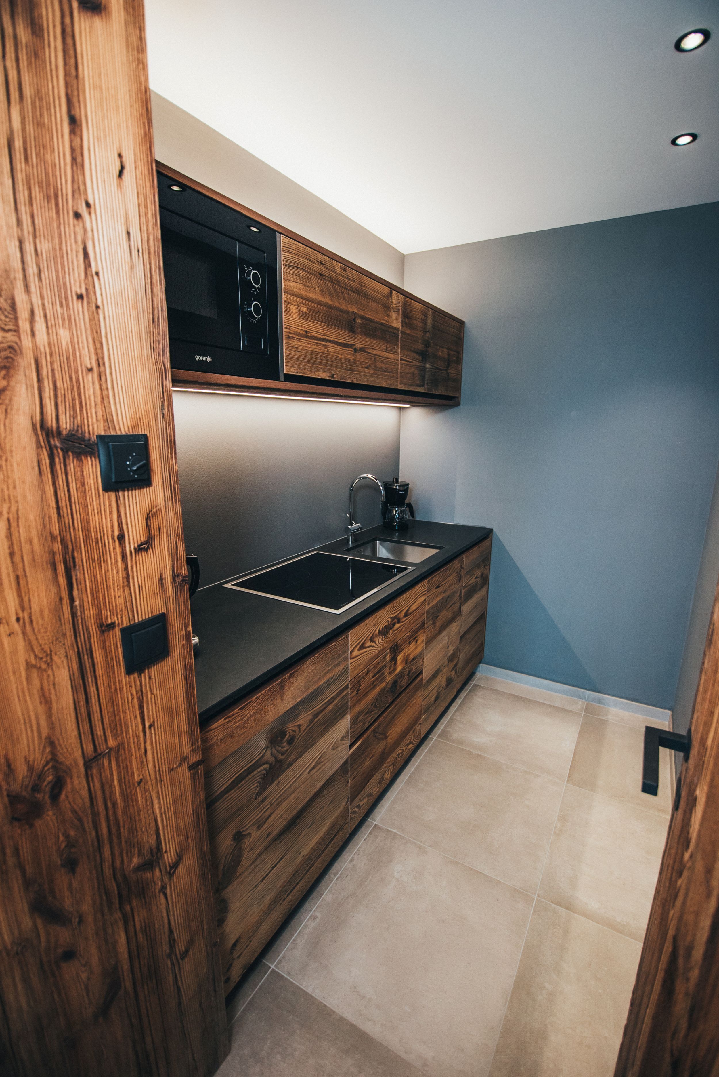 A modern kitchen with wooden cabinetry, a black countertop, and a built-in microwave.